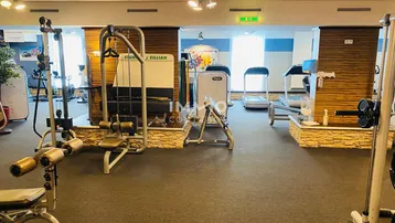 Gut ausgestatteter Fitnessbereich mit verschiedenen Kraft- und Cardiogeräten auf dunklem Bodenbelag.