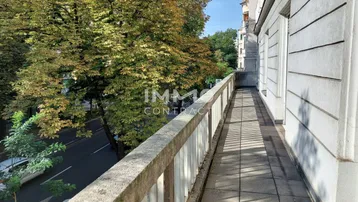 Langer Balkon mit Fliesenboden und Blick auf die von Bäumen gesäumte Straße.