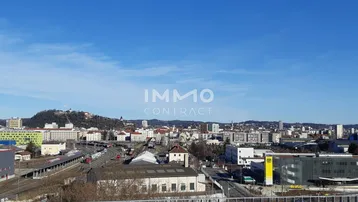 Weitläufiger Panoramablick über die Stadt mit Bergen im Hintergrund unter klarem Himmel.