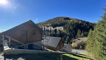 Chalet im Bau mit Holzelementen und Blick auf die umliegende Berglandschaft an einem sonnigen Tag.