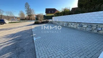 Gepflasterter Außenparkplatz mit markierten Stellflächen und einer Steinmauer im Hintergrund unter blauem Himmel.