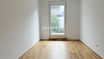 Helles Schlafzimmer mit Parkettboden und Zugang zu einem französischen Balkon.