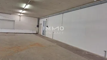 Großer, leerer Gewerberaum mit Betonboden, weißen Wänden und effizienter Deckenbeleuchtung.