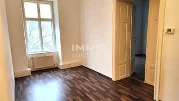 Heller Raum mit dunklem Laminatboden und einem großen Fenster, das viel Tageslicht hereinlässt.