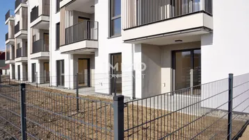 Moderne Fassade eines Neubaus mit Balkonen und Terrassenzugängen im Erdgeschoss.
