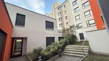 Außenansicht eines modernen Gebäudekomplexes mit Treppenaufgang und begrüntem Innenhof.