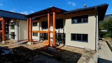 Rückansicht des Neubaus mit Terrassenbereich und Blick auf die umliegende Natur.