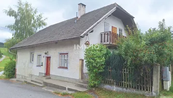 Traditionelles Haus mit Balkon und Satteldach, umgeben von ländlicher Natur und Hügeln.