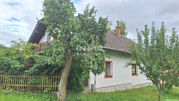 Ländliches Haus mit Satteldach und Gartenbereich, umgeben von Bäumen und grüner Landschaft.