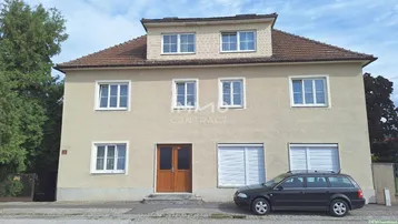 Vorderansicht eines Mehrfamilienhauses mit beiger Fassade und Satteldach, ein Auto parkt davor.