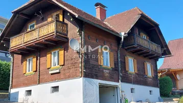 Traditionelles Holzhaus mit Satteldach, Balkonen und integrierter Garage unter blauem Himmel.