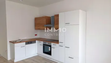 Moderne Einbauküche mit weißen Schränken, Holzarbeitsplatte und integrierten Geräten in einem hellen Raum.