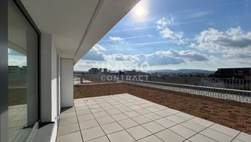 Große Dachterrasse mit hellen Fliesen, begrüntem Bereich und weitem Blick über die Landschaft.