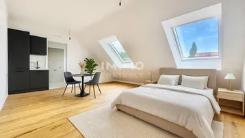 Helles Dachzimmer mit Bett, kleiner Küchenzeile und Essbereich unter schrägen Decken und Dachfenstern.