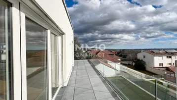Geräumige Terrasse mit Fliesenboden, Glasgeländer und weitem Blick über die Umgebung.