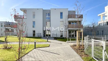 Modernes Mehrfamilienhaus mit heller Fassade, Balkonen und gepflegten Grünflächen.