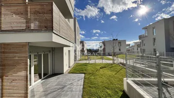 Moderne Wohnanlage mit sonniger Terrasse und angrenzender Rasenfläche unter blauem Himmel.