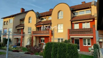 Mehrfamilienhaus mit mehreren Balkonen und gepflegter Gartenanlage bei Sonnenuntergang.