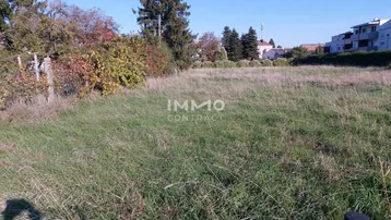 Großes, unbebautes Grundstück mit Grasfläche und Bäumen im Hintergrund, umgeben von Wohnbebauung.