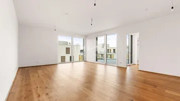 Geräumiges, helles Zimmer mit Holzboden und großen Fenstern, die viel Tageslicht hereinlassen.