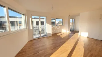 Helles Wohnzimmer mit Parkettboden und Zugang zu einem Balkon, durchflutet von natürlichem Sonnenlicht.
