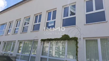 Fassade eines Geschäftsgebäudes mit vielen Fenstern, Kletterpflanzen und einem hellen Anstrich.