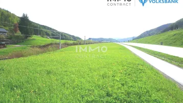Weitläufiges grünes Grundstück neben einer Straße mit malerischer Berglandschaft im Hintergrund.