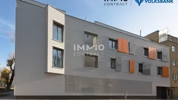 Moderne Fassade eines Wohngebäudes mit grauen Paneelen und farbigen Akzenten unter blauem Himmel.