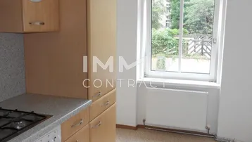 Einfache Küche mit hellen Holzschränken, Gasherd und einem Fenster mit Blick ins Grüne.