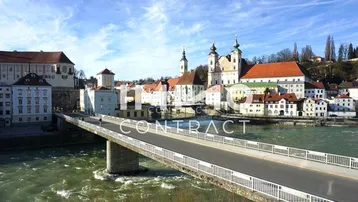 Panoramablick auf eine historische Stadt am Fluss mit Brücke und traditionellen Gebäuden unter blauem Himmel.