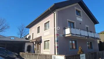 Mehrstöckiges Wohnhaus mit Balkon und Carport unter blauem Himmel.