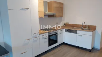 Moderne Einbauküche mit weißen Schränken, Holz-Arbeitsplatte und integrierten Geräten in hellem Raum.