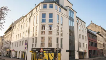 Modernes Eckgebäude mit großen Fenstern und Geschäftsflächen im Erdgeschoss an einer Stadtstraße.