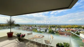 Geräumiger Balkon mit Holzboden, Sitzgelegenheiten und weitem Blick über die Stadt und Landschaft.