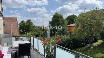 Möblierter Balkon mit Esstisch und Pflanzen, bietet einen weiten Blick ins Grüne und auf die Umgebung.