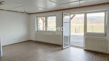 Helles Wohnzimmer mit Laminatboden, Heizkörpern und Zugang zu einer Außenterrasse mit Weitblick.