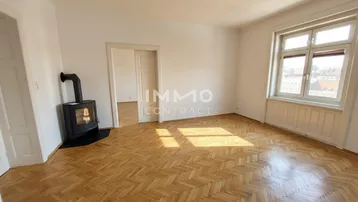 Helles Wohnzimmer mit Fischgrätparkettboden, Kaminofen und Tageslicht durch ein großes Fenster.