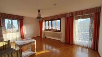 Helles Wohnzimmer mit Parkettboden, großen Fenstern und einem Kronleuchter, der den Raum erhellt.