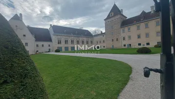 Historisches Schlossgebäude mit weitläufigem Kiesweg und gepflegtem Rasenbereich unter bewölktem Himmel.