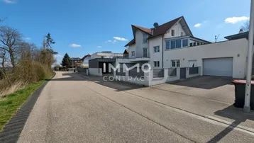 Weißes Wohnhaus mit Garage und gepflasterter Einfahrt an einer ruhigen Straße.