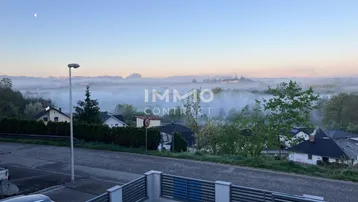 Weitläufiger Blick über eine neblige Landschaft mit Häusern und Bergen am Horizont.