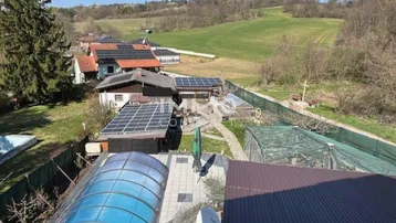 Weitläufiger Blick auf das Anwesen mit Solaranlagen auf den Dächern und grüner Hügellandschaft im Hintergrund.