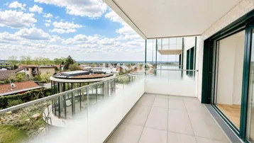 Geräumiger Balkon mit Fliesenboden, Glasgeländer und weitem Blick über die Umgebung.