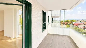 Heller Balkon mit Glasgeländer und Blick auf die umliegende Wohngegend und die Ferne.