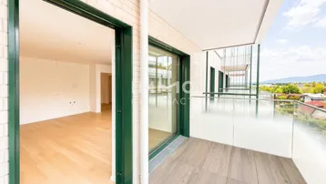 Geräumiger Balkon mit Holzbodenfliesen und Glasgeländer, mit Zugang zu einem hellen Innenraum.
