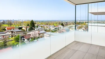 Geräumiger Balkon mit Glasgeländer und weitem Blick über die Stadt und grüne Umgebung.