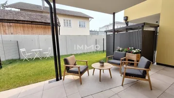 Gepflasterte Terrasse mit modernen Sitzgelegenheiten und angrenzendem Rasenbereich, umgeben von einer Mauer.