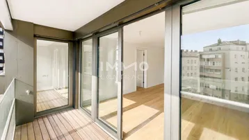 Geräumiger Balkon mit Holzboden und Glasschiebetüren, der Zugang zu einem hellen Innenraum bietet.