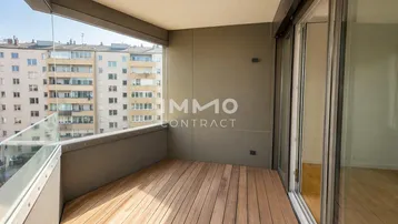 Moderner Balkon mit Holzfußboden und Glasbrüstung, bietet einen weiten Blick auf die Stadt.