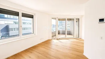 Helles, leeres Wohnzimmer mit Parkettboden und Zugang zu einem Balkon, bietet viel natürliches Licht.